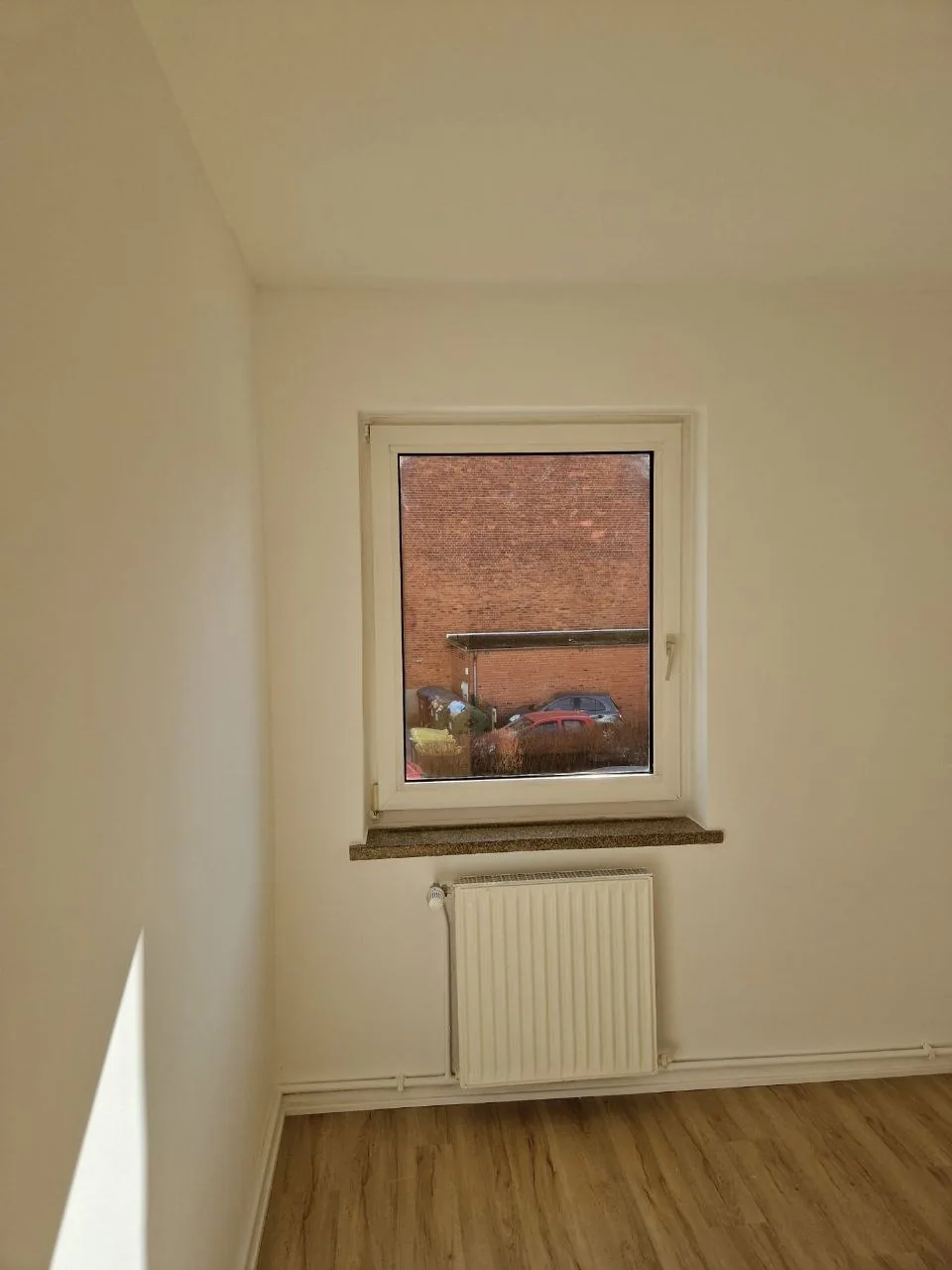 Heller Wohnraum mit weißen Wänden, Fenster und Laminatboden